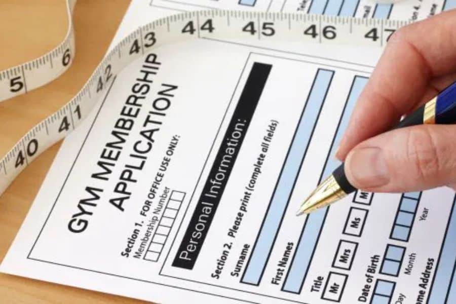 Close up of a "GYM MEMBERSHIP APPLICATION" form being filled out with a pen beside a measuring tape. This fits content about save money by reviewing recurring subscriptions and fitness costs before signing up.