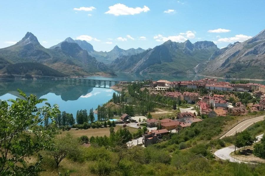 Mountain lake reflects sharp peaks behind a lakeside village with red roofs and a long bridge stretching across the water. Scenic stop near hiking trails in Europe.