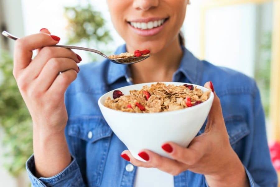 A woman in a blue denim shirt eating a bowl of cereal