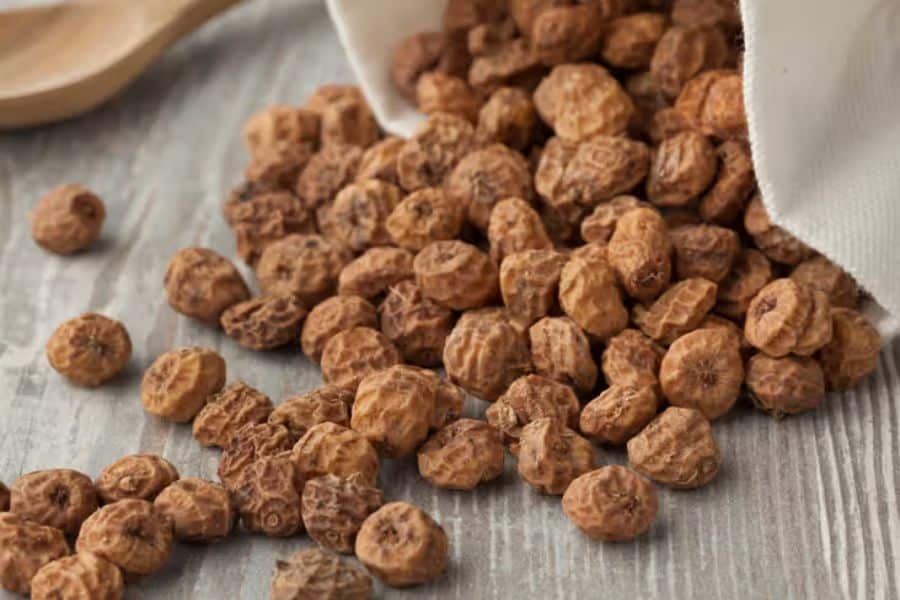 Wrinkled tiger nuts spill from a white cloth bag onto a light wooden surface. This close view introduces a fiber rich whole food that may appear in a memory decline nutrition article.