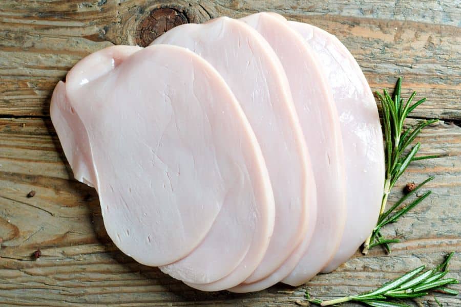 Several pale slices of turkey breast arranged on a rustic wooden board with rosemary sprigs at the side. The image emphasizes lean turkey as a plain protein option in a list of healthy foods.