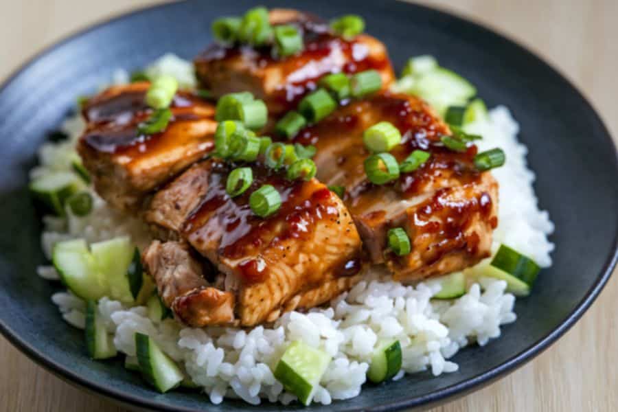 Glazed salmon pieces served over white rice with chopped cucumber and sliced green onions in a dark bowl. This protein rich meal works well in content about satisfying foods and hunger hormones.