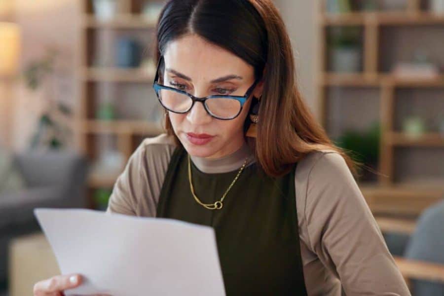 Woman wearing glasses reads a document at a desk in a home office setting. This works for content about reviewing loan terms or checking paperwork before applying for no credit check loans.