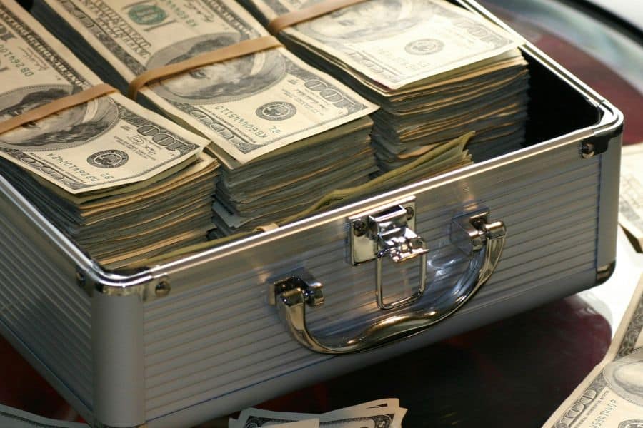 Open silver briefcase filled with thick stacks of one hundred dollar bills bundled with rubber bands. This close up photo suggests a large cash reserve or savings pool related to a retirement fund.