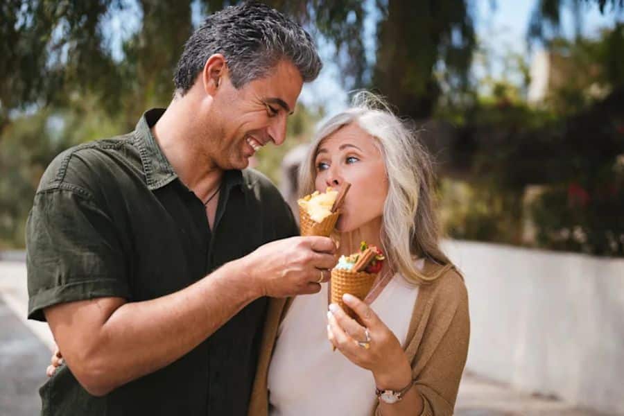 Smiling older couple outdoors sharing ice cream cones and looking at each other warmly. The photo suggests enjoying simple moments together as part of long term financial strategies for retirement.