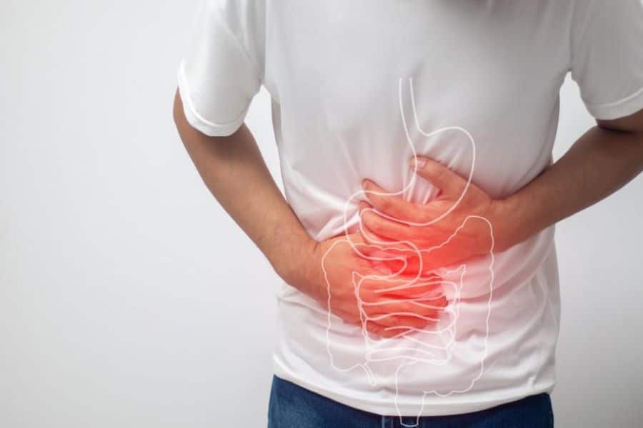 A person in a white shirt clutches their stomach with a red highlighted overlay showing digestive organs. The visual represents stomach discomfort that may occur when someone is low in magnesium.
