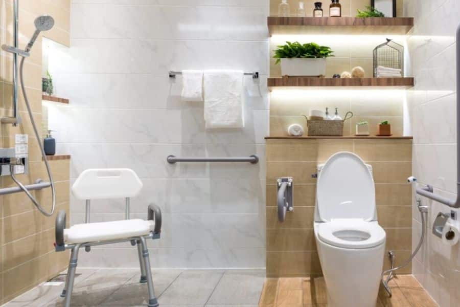 Accessible bathroom with a shower chair. Grab bars beside the toilet and shower. Open shelving with towels and toiletries. The scene highlights home safety upgrades that may factor into retirement financial strategies.