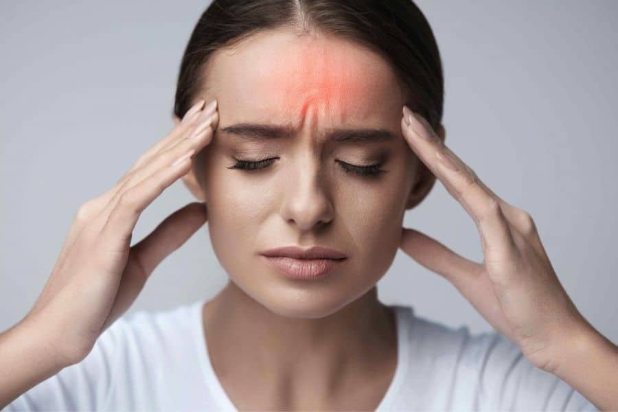 A close up of a woman pressing her temples with a red highlight across her forehead indicating pain. The image represents headaches that may be a symptom of being low in magnesium.