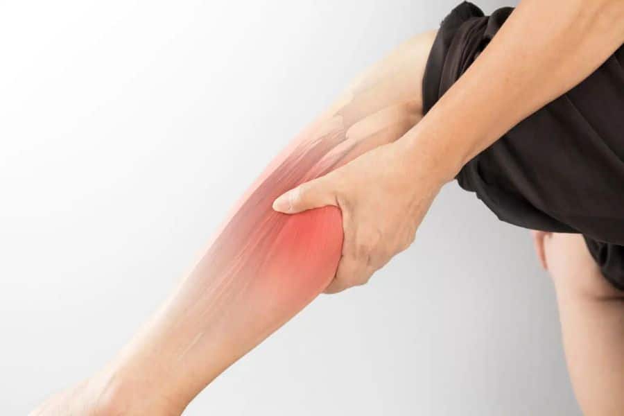 A person grips their calf muscle with a red highlighted area showing pain or cramping. Muscle cramps like this are often associated with being low in magnesium.