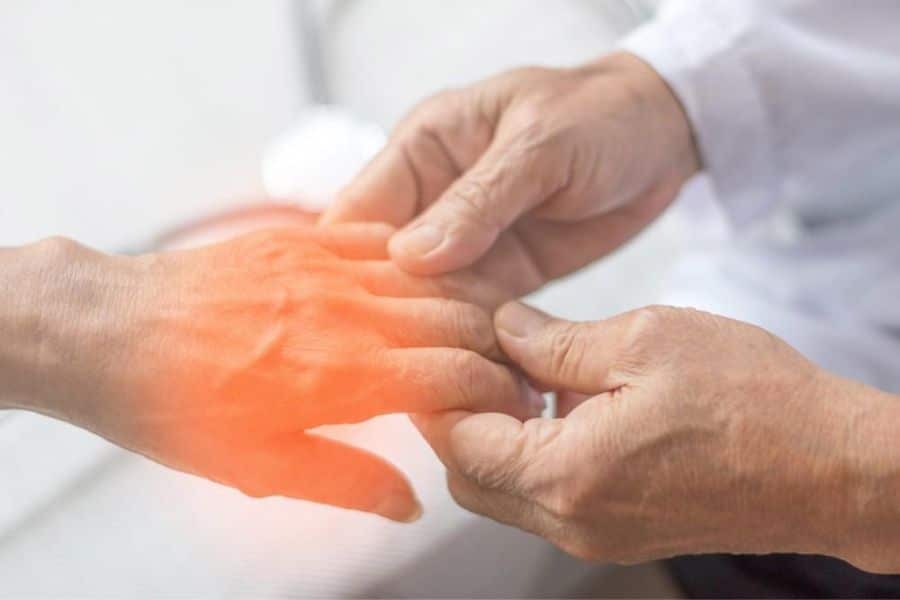 Close up of hands where one hand is being held and highlighted in red to indicate joint pain. The discomfort shown can be linked to muscle and nerve issues from being low in magnesium.