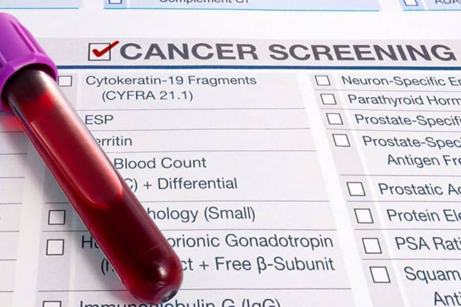 Close up of a blood sample tube resting across a medical form labeled "CANCER SCREENING" with checkboxes and test names underneath. This connects to Medicare benefits by showing preventive screening and lab testing services.