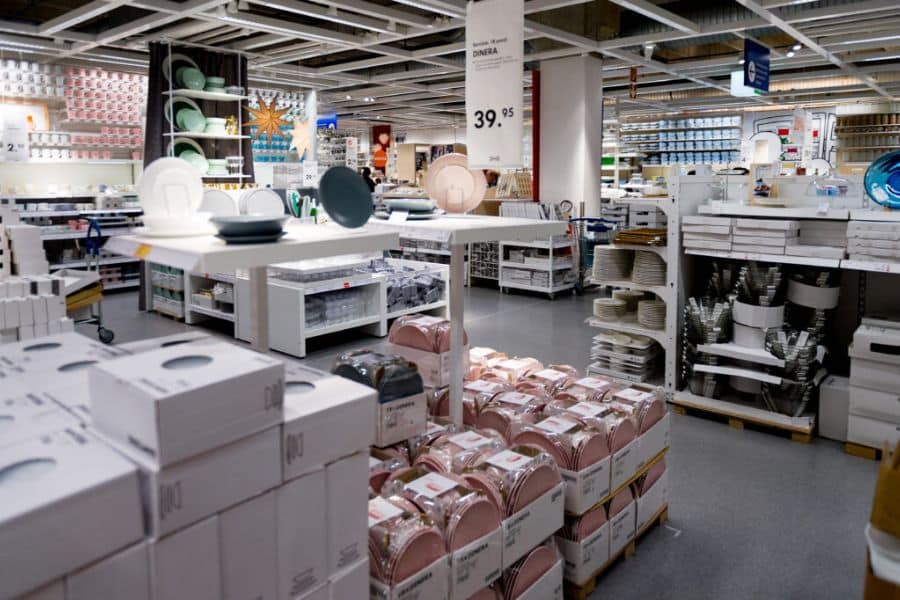 Bright home goods showroom with tables of dishes, stacked boxed products, and store displays arranged across a large retail floor. Visible signage reads "DINERA" and "39.95", which fits retailer tricks content about store layouts and price anchoring in large retail spaces.