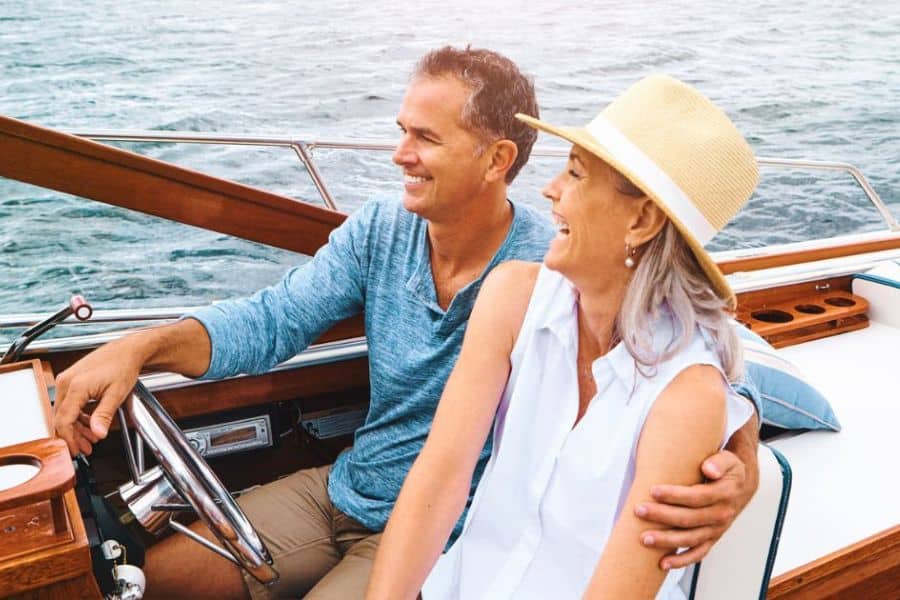 Happy couple sitting close together on a boat with ocean water behind them. The scene conveys leisure and connection during retirement after building financial strategies that support travel and free time.