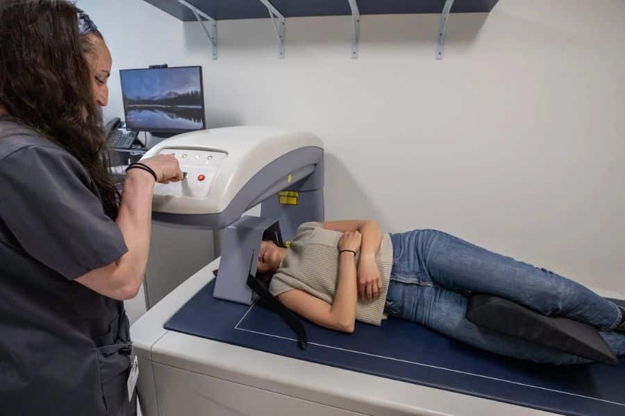 Technician operating a scanning machine while a patient lies on an exam table. The scene shows a diagnostic test that may be part of Medicare covered care.