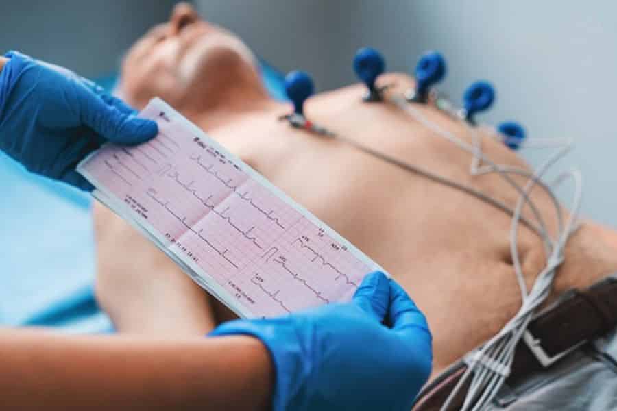 Healthcare worker holding an EKG printout while a patient is connected to chest electrodes. The test is being reviewed during a cardiac exam.