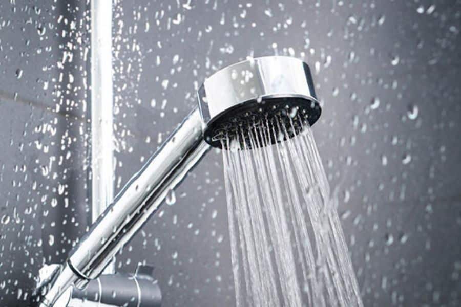 Close up of a shower head spraying water against a glass wall covered in droplets. The image represents sustainable switches such as water saving shower habits and reducing household water consumption.