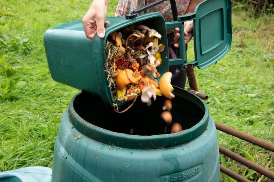 Kitchen scraps and food waste being emptied into a green outdoor compost bin on grass as part of a hot composting setup for organic recycling.