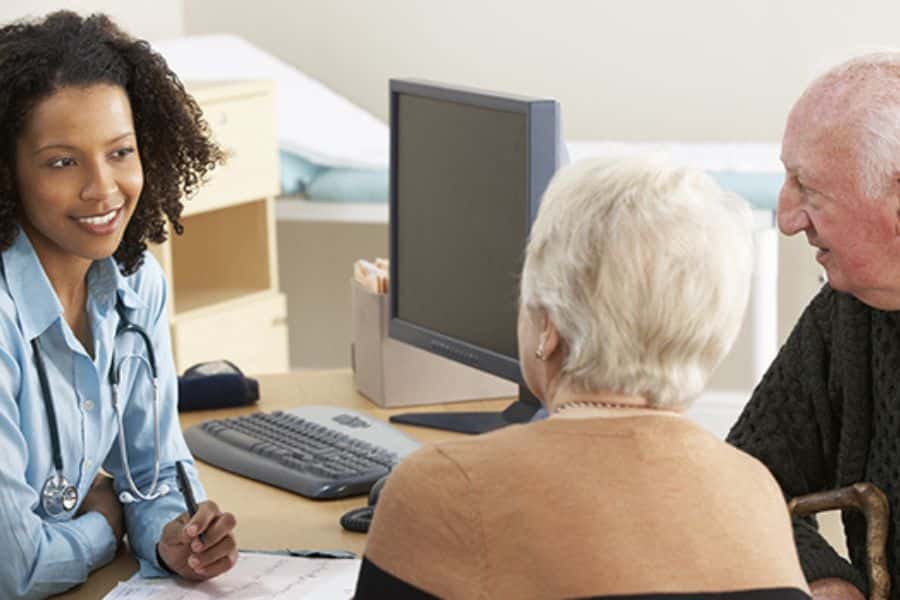 Doctor speaking with an older couple during an office appointment. The consultation shows a patient and caregiver discussing healthcare needs.