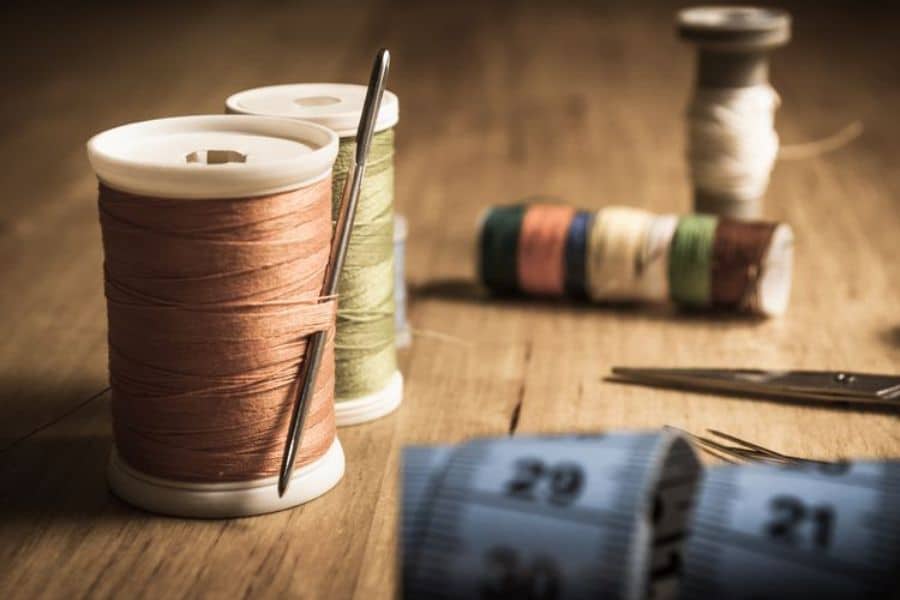 Spools of thread, sewing needles, scissors, and a measuring tape arranged on a wooden table. The sewing supplies symbolize sustainable switches such as repairing clothing instead of replacing damaged items.