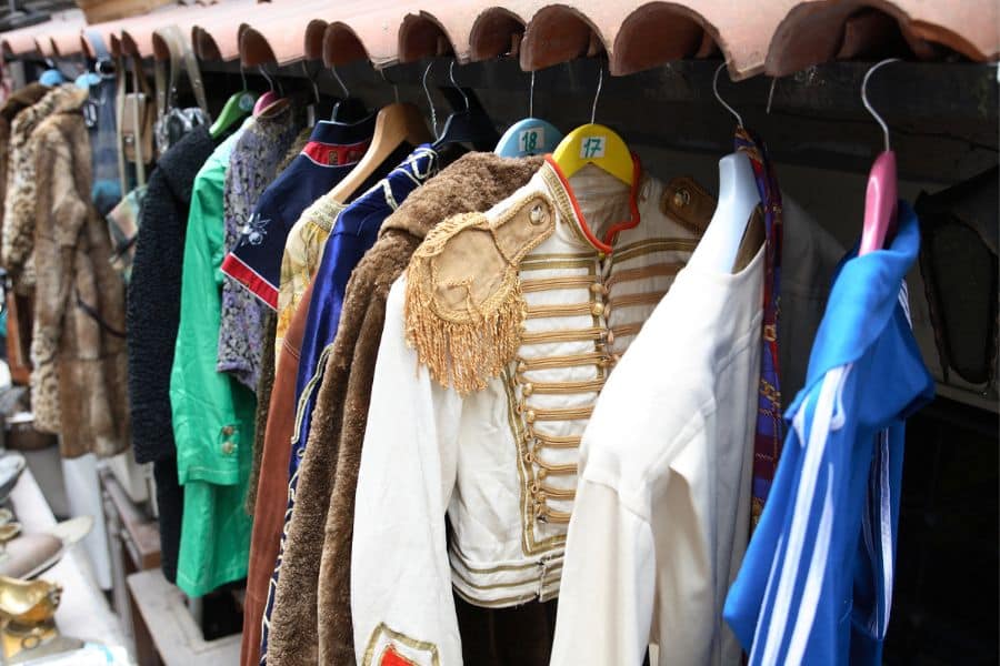 A clothing rack holds vintage costumes including jackets uniforms and coats on hangers. The collection suggests costume rentals or resale as a simple side hustle.