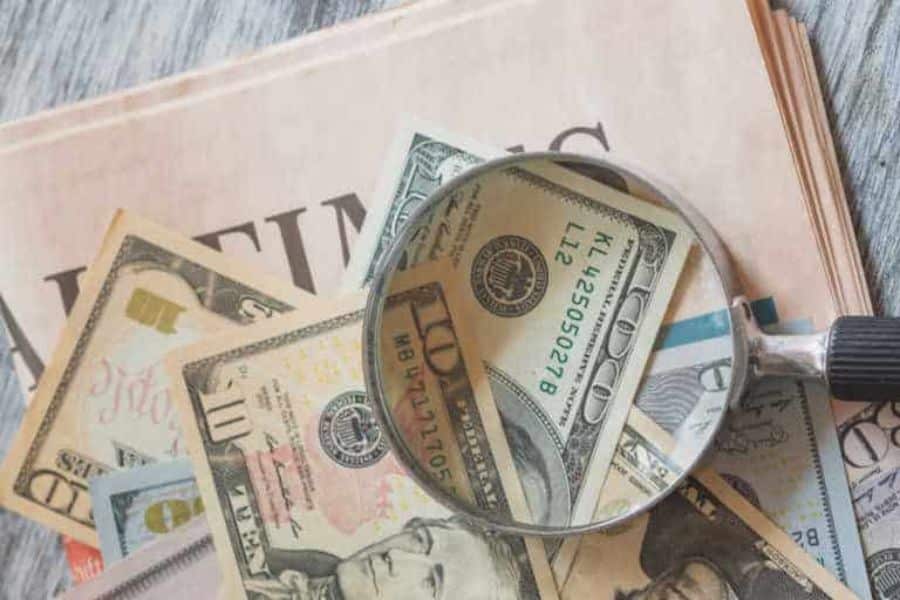 Magnifying glass over cash and financial papers to show looking for savings for retirees.