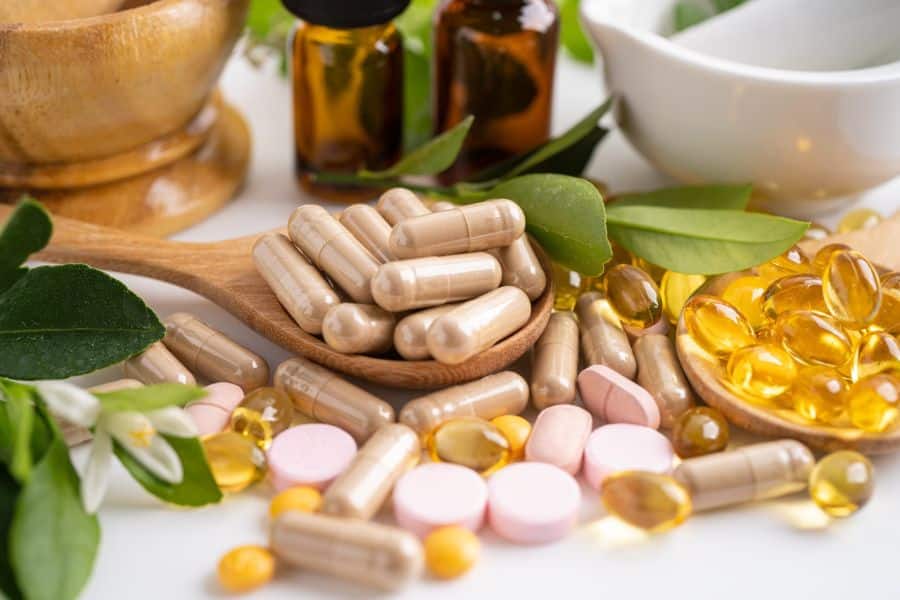 Assortment of capsules, soft gels, and herbal ingredients arranged with glass bottles and a mortar and pestle on a clean surface. Natural supplements often associated with reverse aging routines and wellness focused skin support.