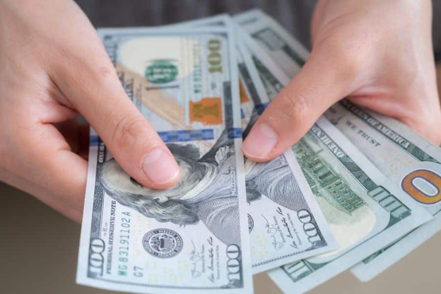 Hands holding and counting several crisp one hundred dollar bills in a close up view. The image symbolizes saving cash, financial planning, and contributing to a savings account.