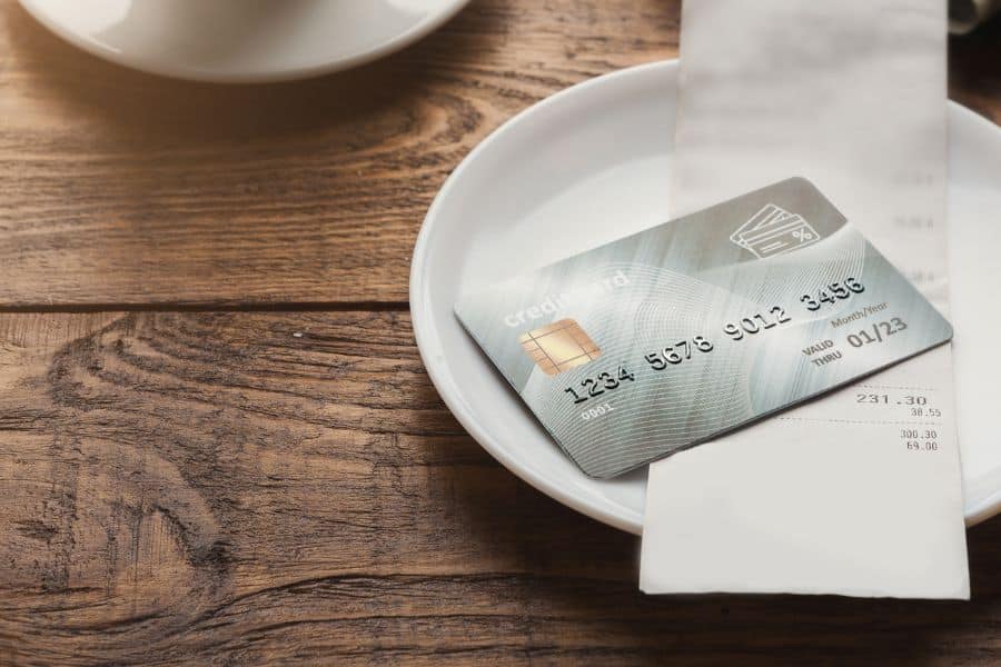 A credit card rests on a restaurant receipt on a small white plate after a meal.