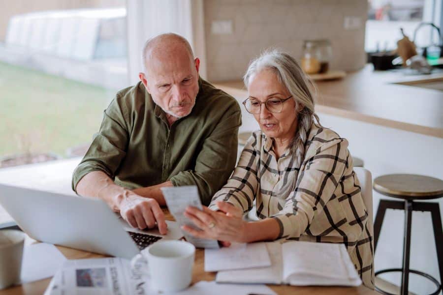 Older couple sitting at a kitchen table reviewing paperwork and bills while discussing debt when you die.