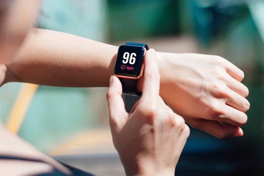 Person tapping a fitness watch on their wrist during a workout. The watch screen reads "96 bpm" with a heart icon to show live heart rate tracking.