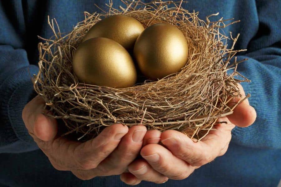 Three golden eggs resting in a straw nest held carefully in both hands. The nest represents protecting long term savings like a retirement fund.