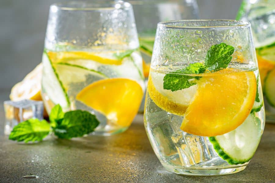 Two chilled glasses of citrus infused water with orange slices cucumber mint leaves and ice. The refreshing drink suggests hydration as part of supporting memory and overall brain health.