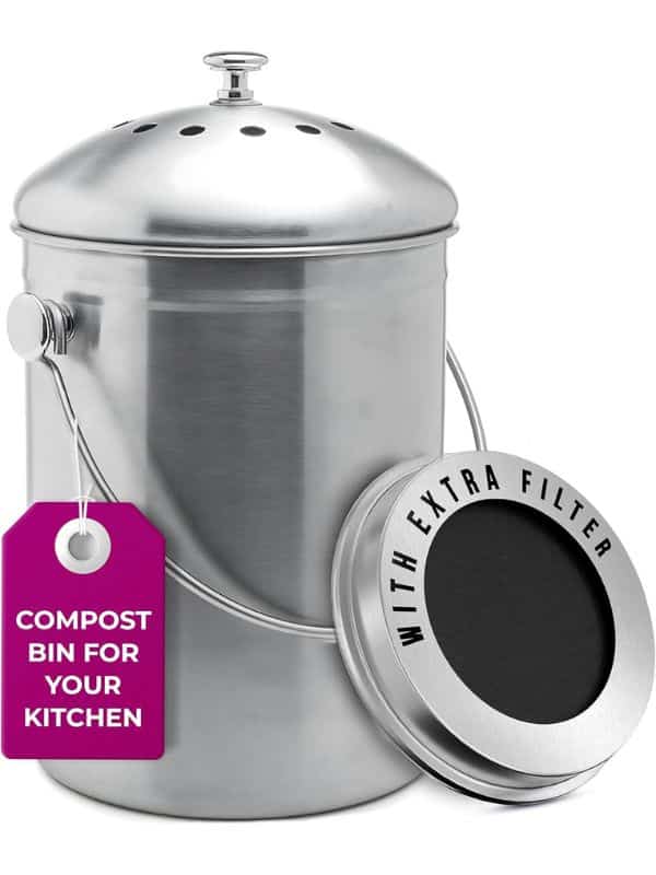 A stainless steel kitchen compost bin with a vented lid and a removable charcoal filter leaning against it. The attached tag reads "COMPOST BIN FOR YOUR KITCHEN" and the filter rim reads "WITH EXTRA FILTER".