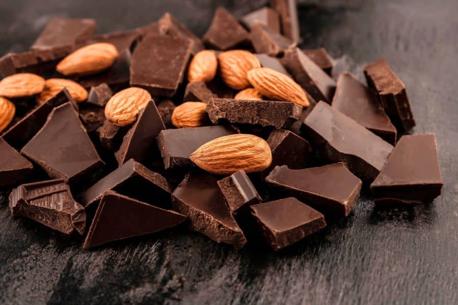 Chunks of dark chocolate mixed with whole almonds on a dark tabletop. A simple sweet and crunchy snack pairing.