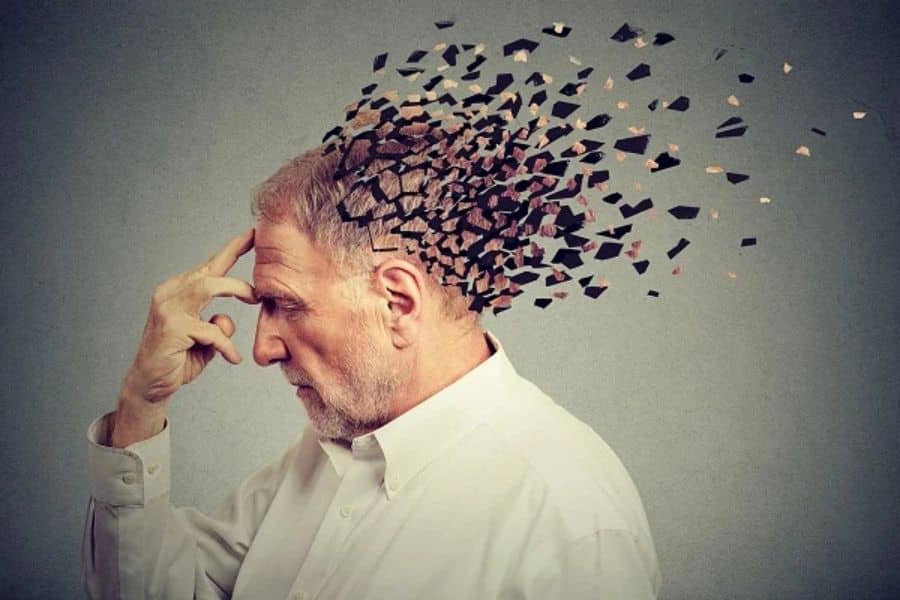 Older man holding his forehead as fragments break away from his head, representing memory loss and Alzheimer’s disease.