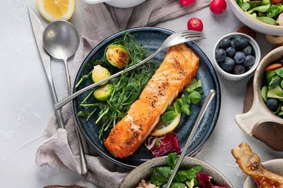 Grilled salmon fillet served with leafy greens, Brussels sprouts, lemon slices, and fresh vegetables on a plate. This anti inflammation meal combines omega 3 rich fish and nutrient dense produce commonly included in an anti inflammatory eating pattern.
