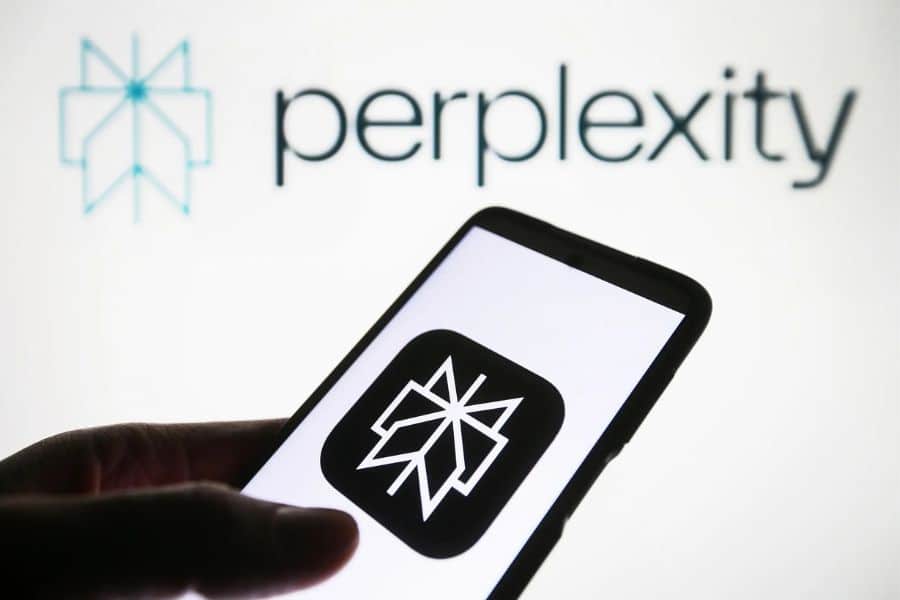 A hand holds a smartphone displaying the Perplexity logo against a background reading "perplexity". The visual represents an artificial intelligence search tool for quickly researching information online.