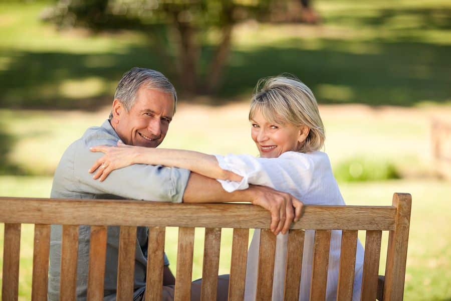 Smiling couple sitting together on a park bench and looking toward the camera in a peaceful outdoor setting. The image represents long term financial planning and retirement strategies, including retirement loophole that can help maximize savings and reduce taxes over time.