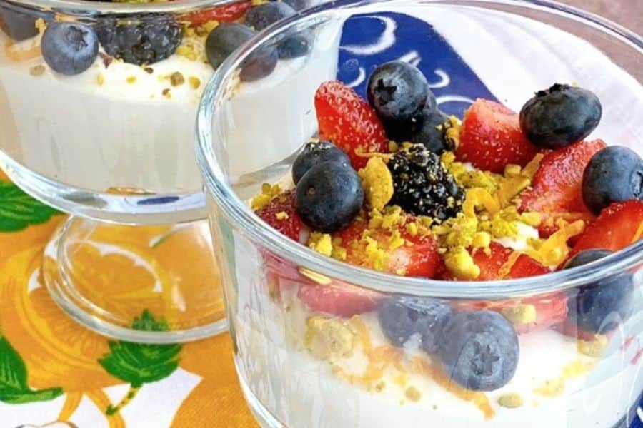 Clear dessert cups filled with creamy yogurt and topped with strawberries. blueberries. blackberries. and crushed pistachios.
