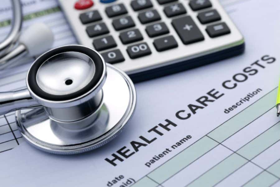 Stethoscope resting on a document labeled "HEALTH CARE COSTS" beside a calculator, illustrating the financial side of healthcare and Medicare planning. The visible form includes the text "HEALTH CARE COSTS," "Patient name," "description," and "date."