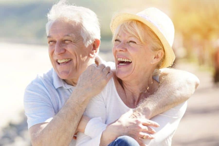 Older couple on a sunny day with arms around each other laughing