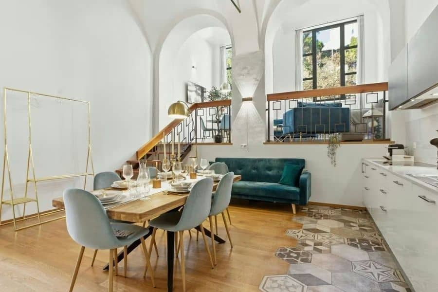 Open dining and living area staged with a set dining table. blue velvet sofa. tall arched ceilings. decorative tile flooring. and bright windows that show how furniture can define the space.