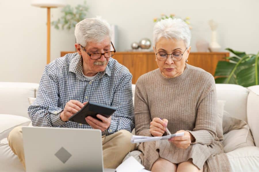 An older couple sitting on a couch with a laptop in front of them looking for tax loopholes for retirees