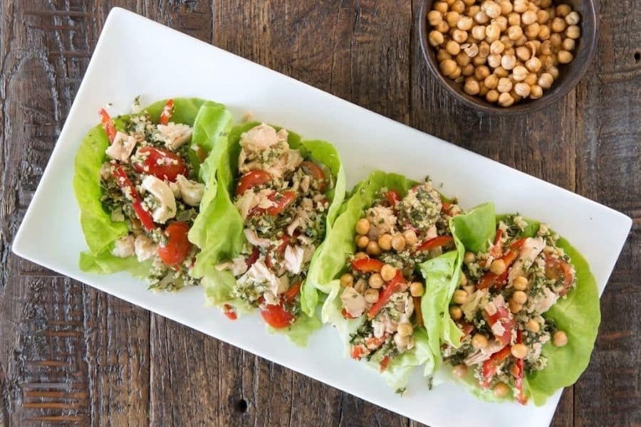 Crisp lettuce cups filled with chicken tomatoes herbs and grains then topped with crunchy chickpeas. A small bowl of roasted chickpeas sits beside the platter.