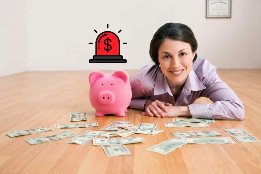 Woman lying on a wooden floor with a pink money box pig with dollar notes around it and a red alarm bell