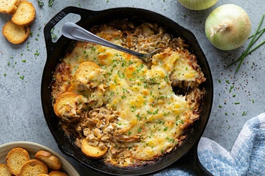 Hot cheesy dip baked in a cast iron skillet and sprinkled with chopped chives. Toasted bread rounds surround the creamy dip for scooping.