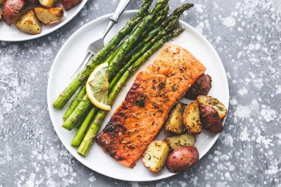 Seared salmon fillet served with roasted red potatoes grilled asparagus and a lemon wedge. The simple plate combines fish and vegetables for a Mediterranean diet inspired dinner.