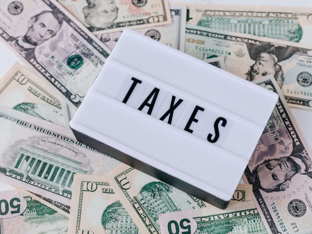 A lightbox reading "TAXES" sits on scattered U.S. dollar bills. The scene represents the tax consequences to consider when planning a Roth conversion.