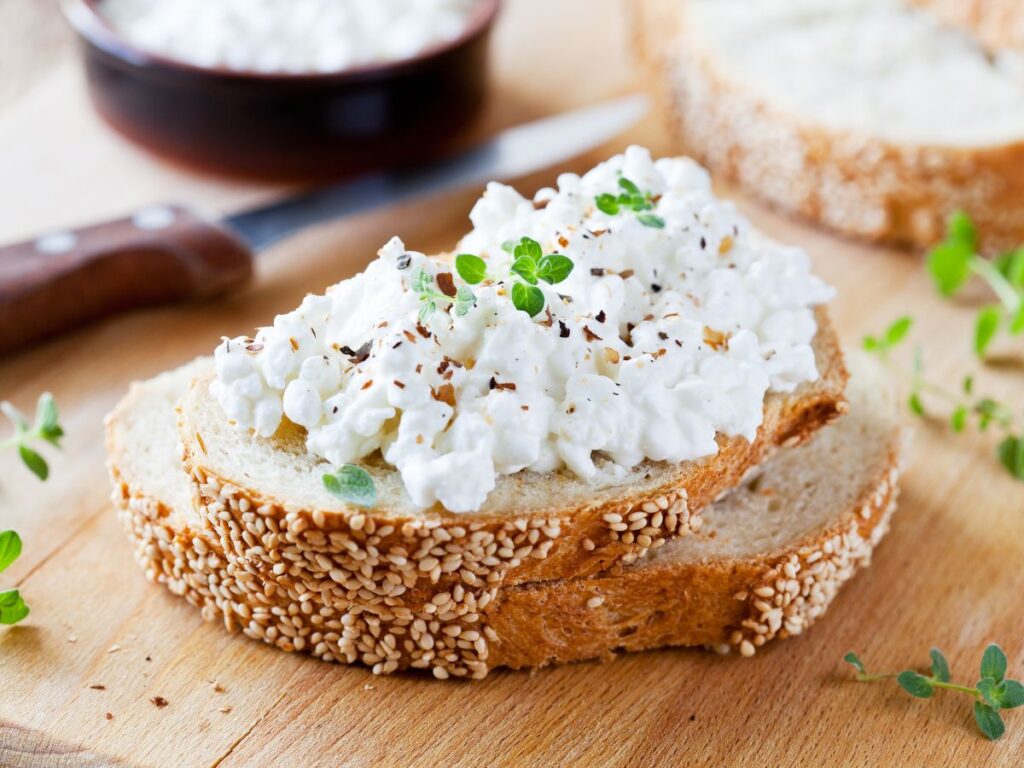 Cottage cheese is piled generously on two slices of seeded bread and topped with fresh herbs and black pepper. The high protein topping makes a simple option for meals designed to help rebuild muscle.