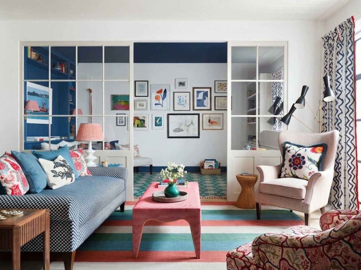 An eclectic living room combines a blue patterned sofa, pink bench, upholstered armchairs, colorful rugs, patterned curtains, and a gallery wall. Layering prints, artwork, and saturated colors creates a playful way to elevate your home decor.